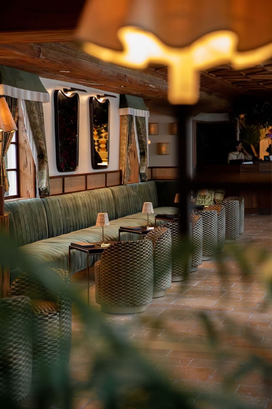Lounge area with green couch, patterned chairs, brick floor, and lit lamps in a restaurant.