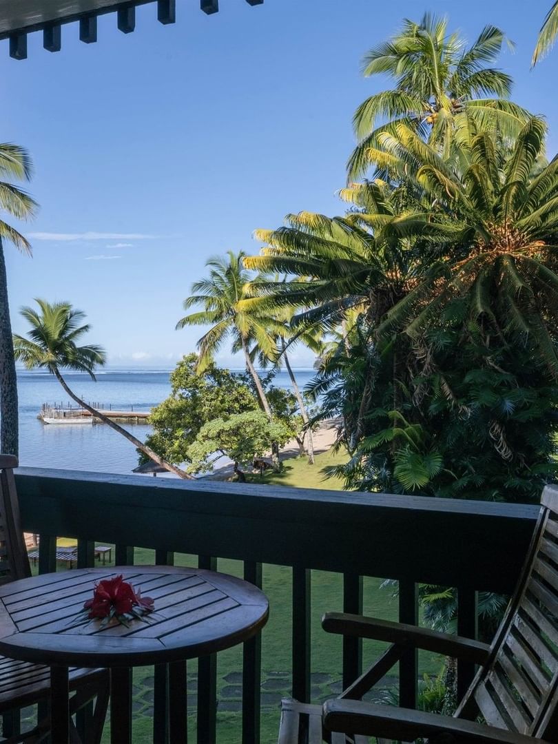 Wooden chairs by a round table on a balcony overlooking the calm blue ocean and palm trees at Warwick Hotels & Resorts