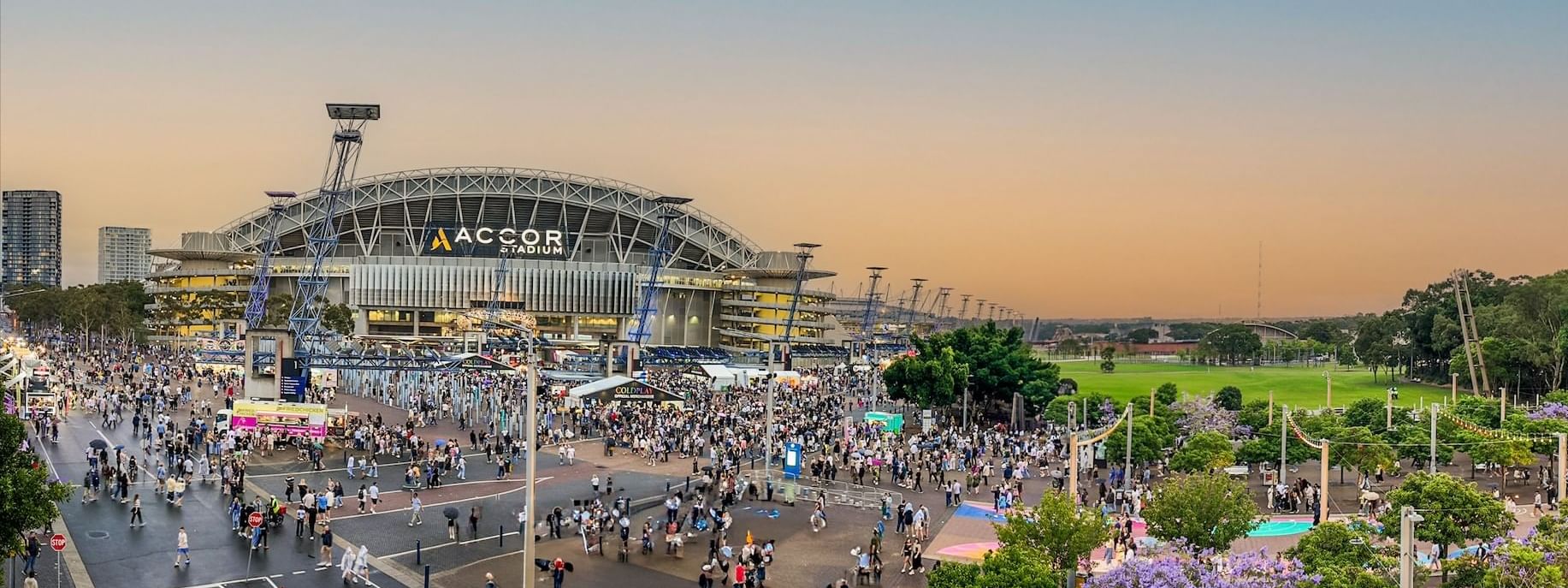 Crowds gathered outside Accor Stadium at dusk, with vibrant skies and bustling atmosphere near Novotel Sydney Olympic Park