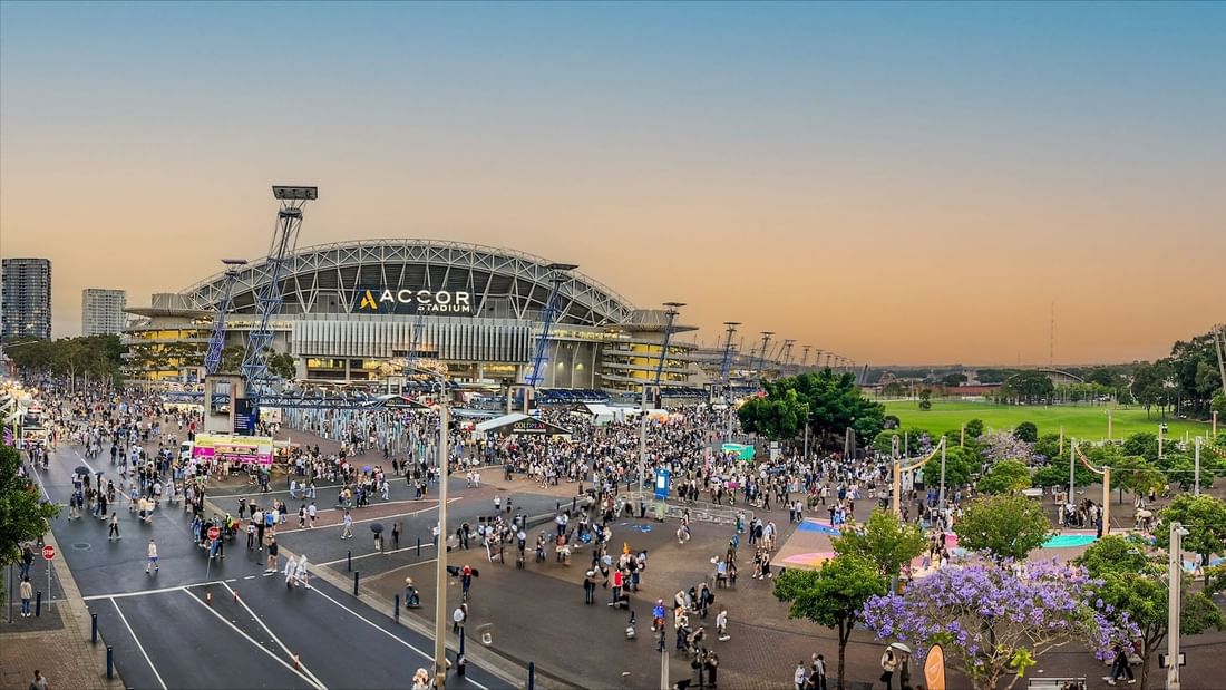 Crowds gathered outside Accor Stadium at dusk, with vibrant skies and bustling atmosphere near Novotel Sydney Olympic Park