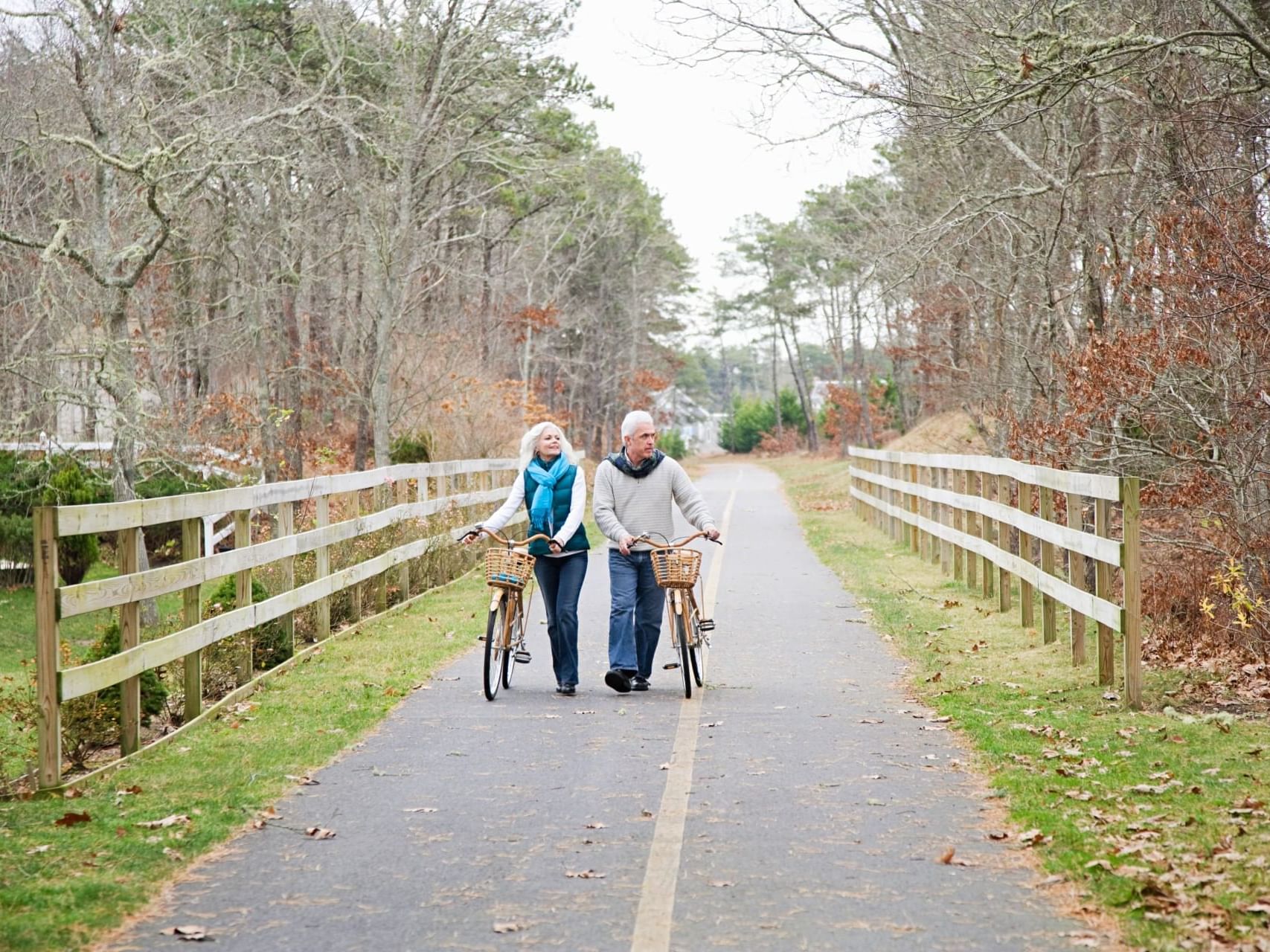 Adult couple walking with bicycles on Cape Cod Rail Trail surrounded by trees near Chatham Tides Resort