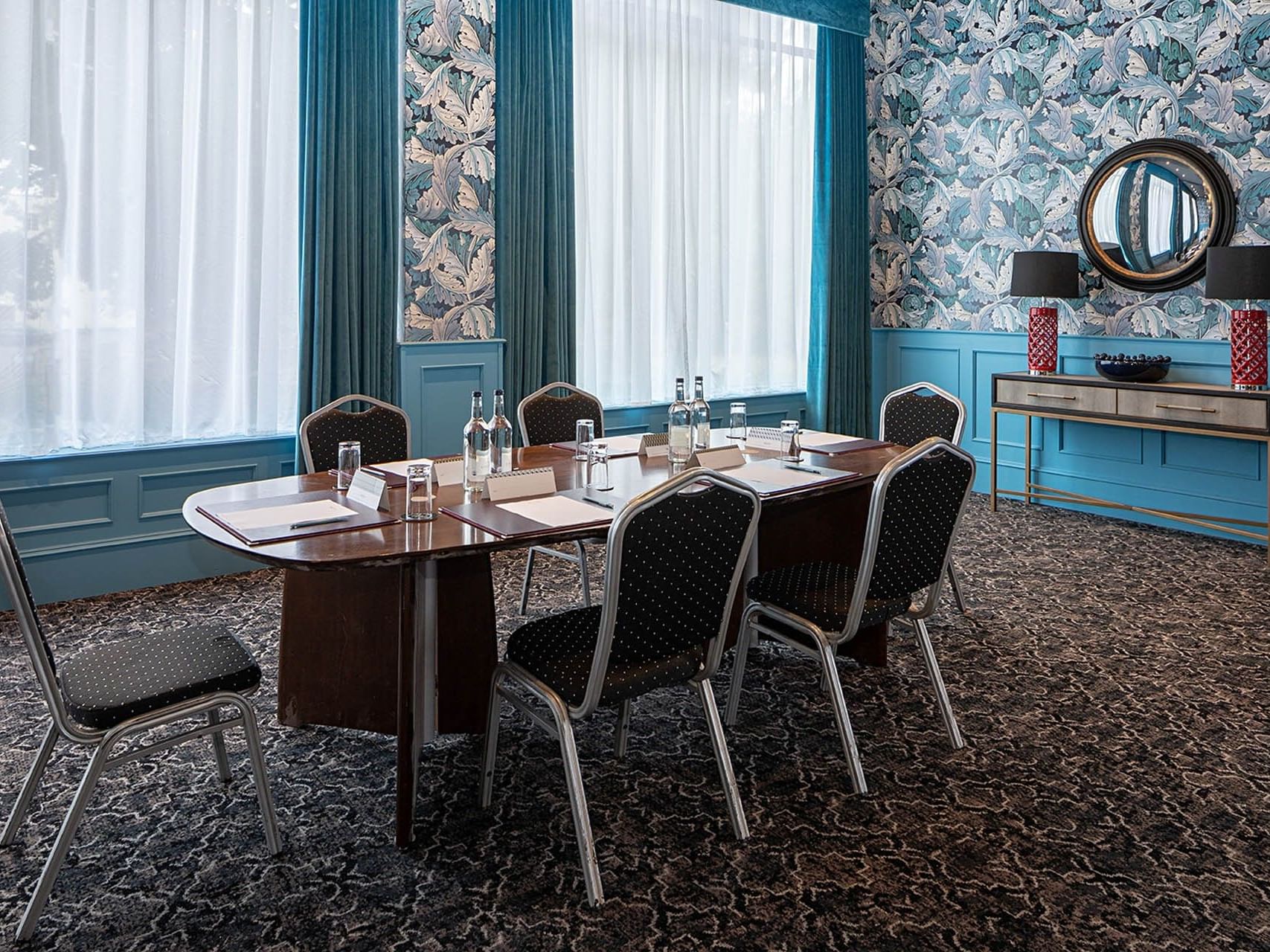 A meeting room with a large table, chairs, and a decorative wall with a mirror and lamps.