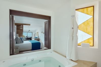 Large bathroom with whirlpool tub, white robe, and mirror reflecting bedroom with ocean view.