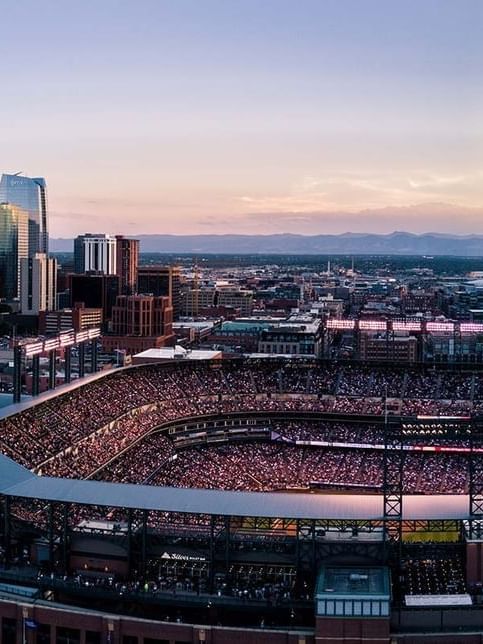 Denver Stadium with Crowded stadium by city buildings under a hazy sunset sky in a valley near Warwick Denver