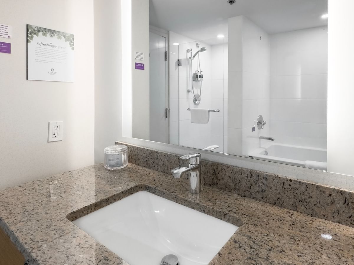Bathroom with granite sink, mirror reflecting bathtub and shower.