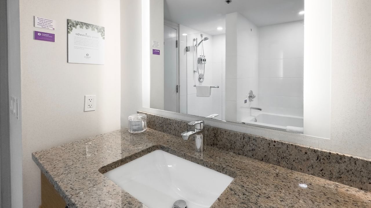 Bathroom with granite sink, mirror reflecting bathtub and shower.