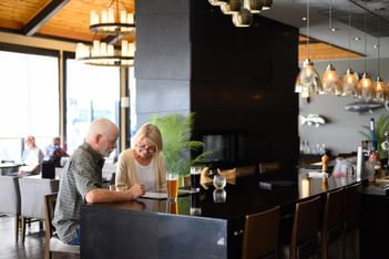 Couple dining near dark bar counter under pendant lights at Rodd Miramichi River, one of the best hotels in Miramichi, NB