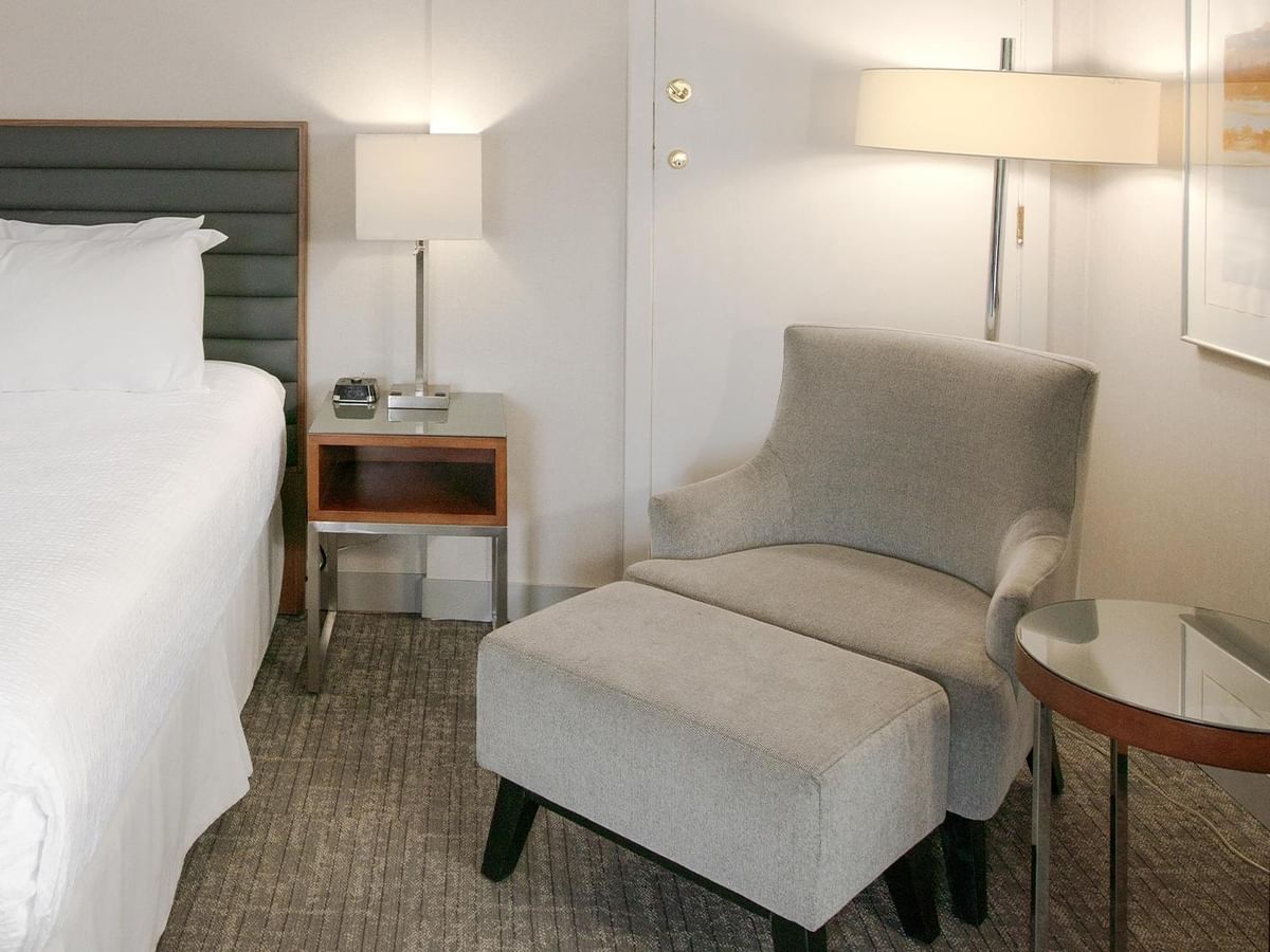 Modern junior suite with queen bed, gray armchair with ottoman, and bedside lamp at Coast Prince George Hotel.