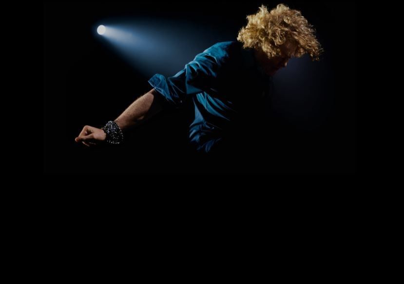 Simply Red singer in dramatic stage lighting during a concert, with a focus on movement and light.