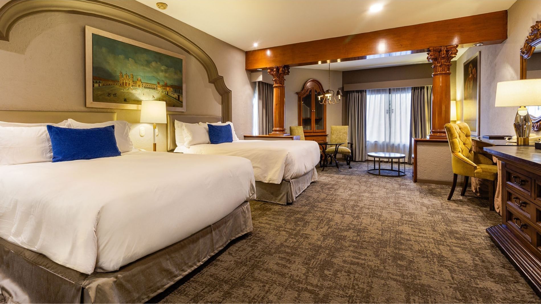2 Double Grand Class beds with blue accents, wood columns, and historical artwork at Quinta Real Guadalajara
