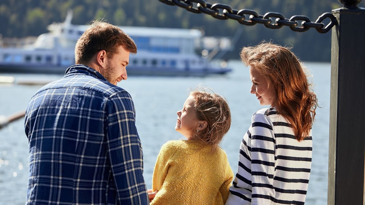 Family of three enjoying a sunny waterfront view with a ferry in the background