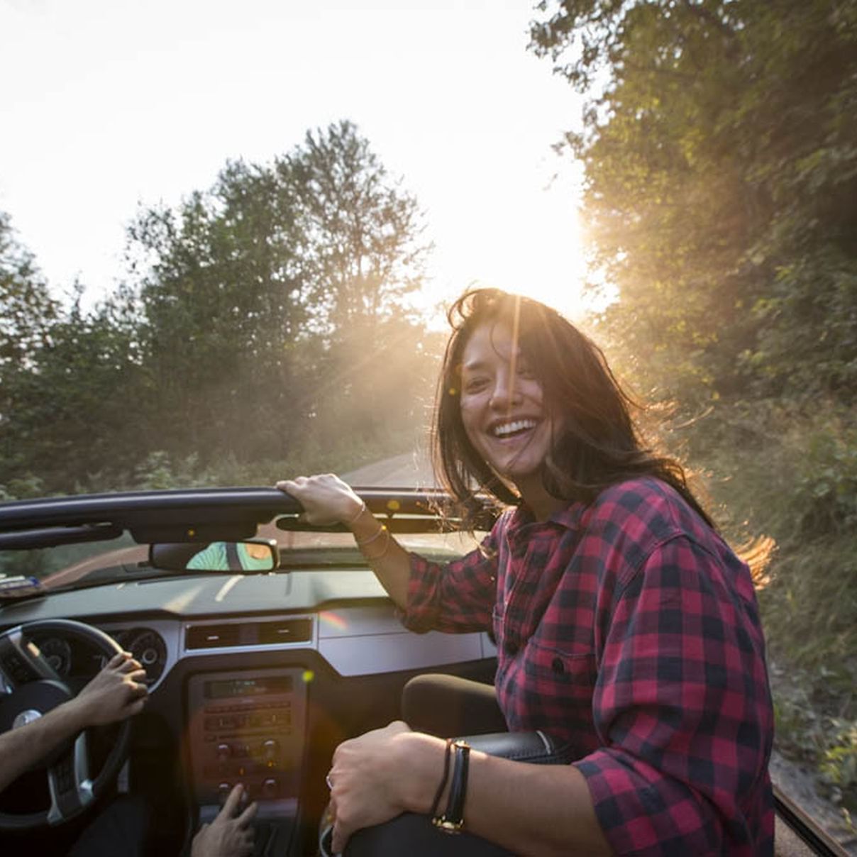 Couple driving a convertible through a forest on a sunny day.