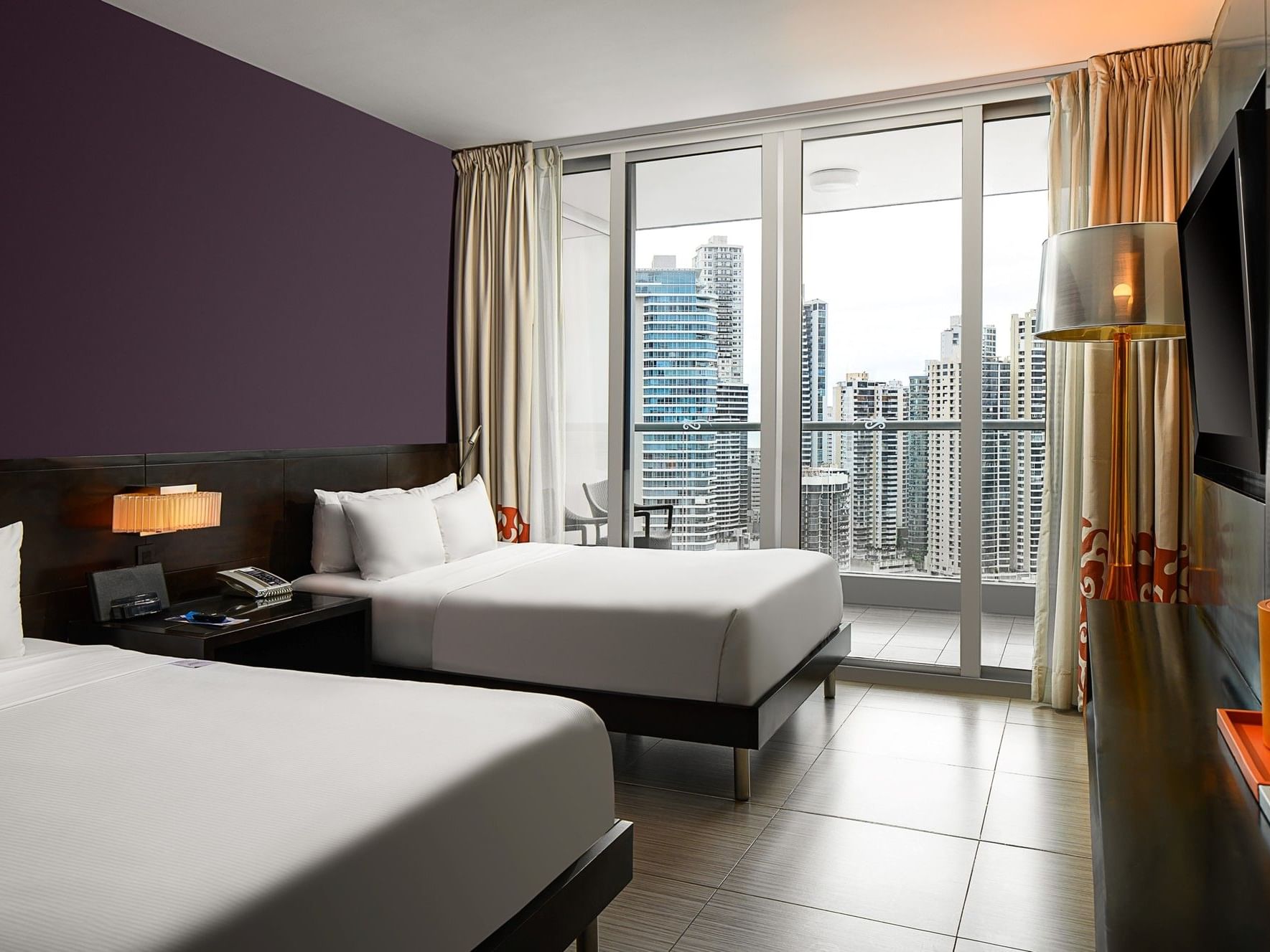Hotel room with two beds, a balcony with city view, and modern furnishings.
