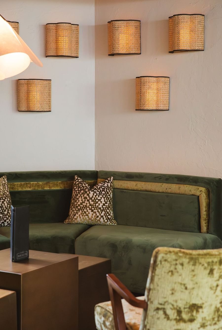 Lobby lounge green couch with pillow and chair in room with wall sconces and coffee table.