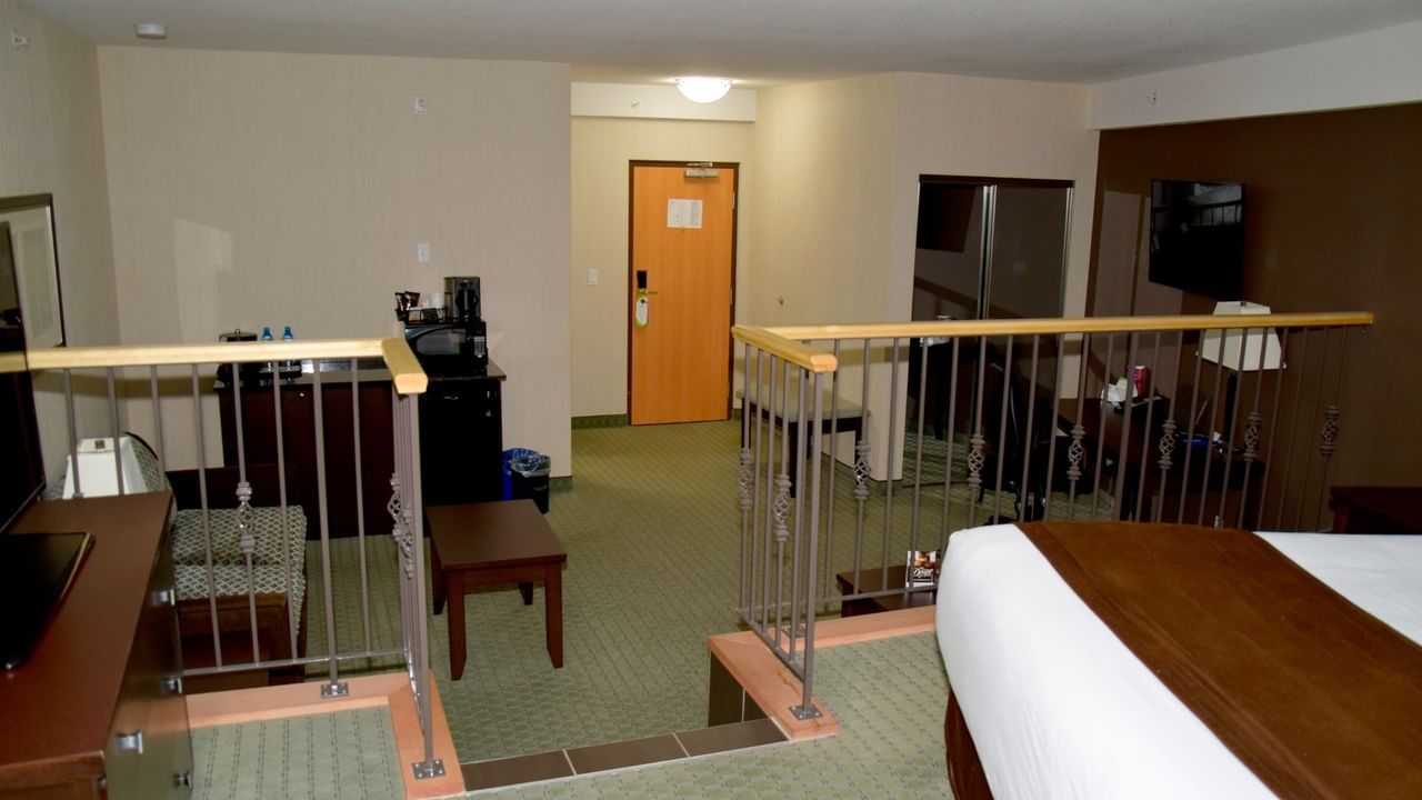 A hotel room with a balcony, a bed, a desk, a coffee maker, and a TV.