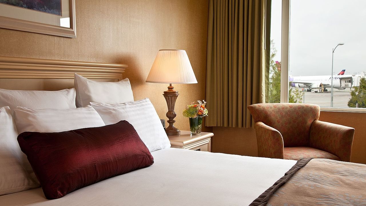 Bed and sofa chair in hotel room with view of airport