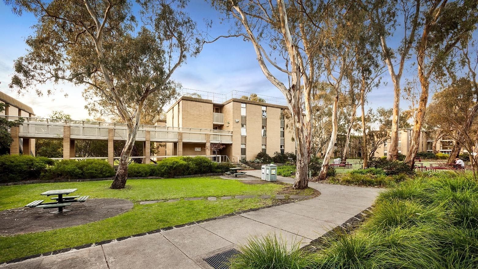 La Trobe University - Glenn College campus view with picnic tables and tall trees.
