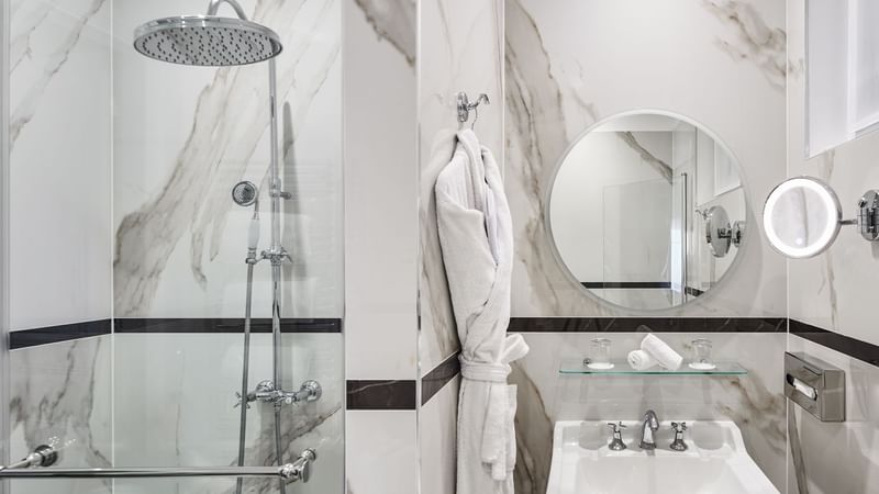 Modern bathroom featuring a glass shower, a round mirror, and marble walls in Executive Room at Hôtel Westminster - Paris