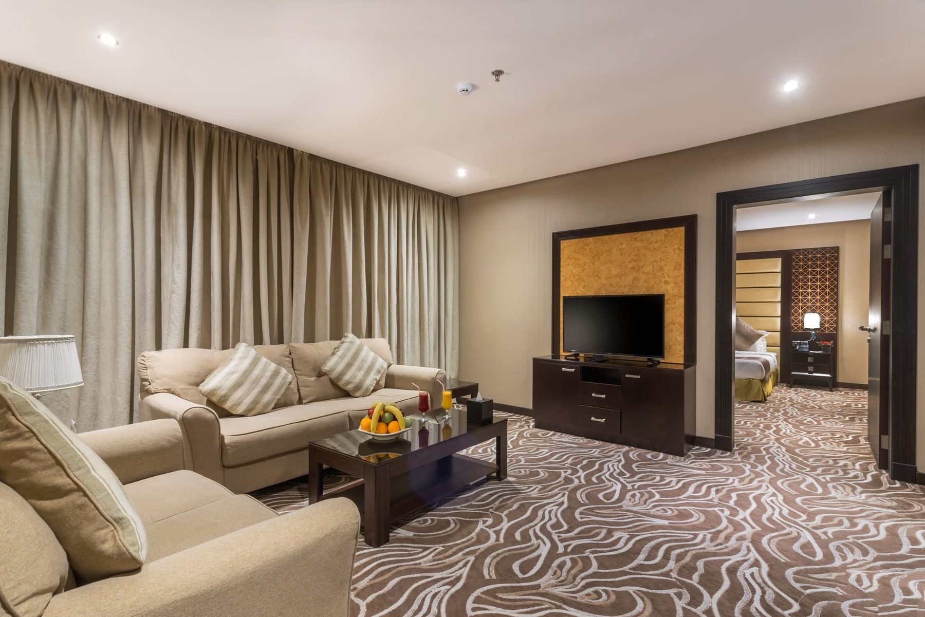 Junior Suite features Beige sofas by a coffee table with fruit under long curtains at Naviti by Warwick Al Khobar