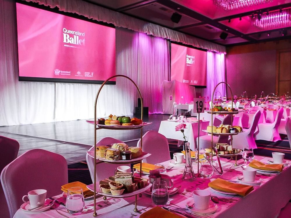 A spacious banquet hall illuminated with pink lighting and featuring food platters on a table at Sofitel Brisbane Central