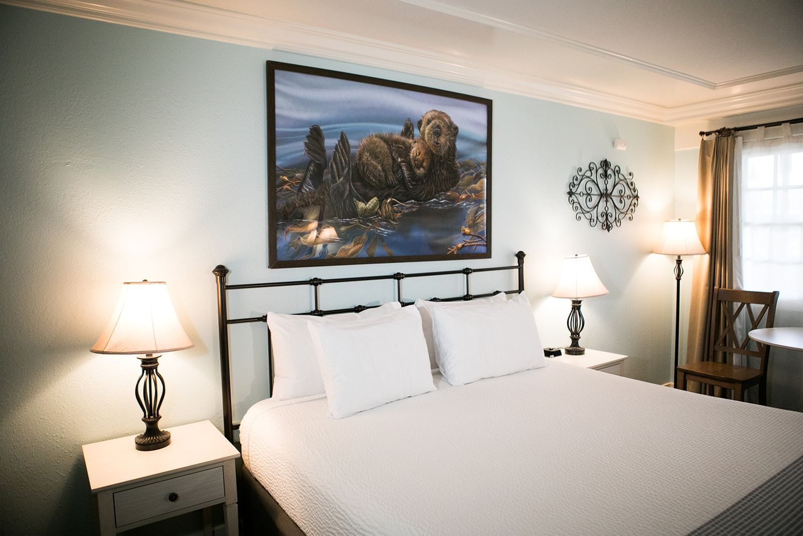 A hotel room with a king-sized bed, two nightstands, and a painting of an otter