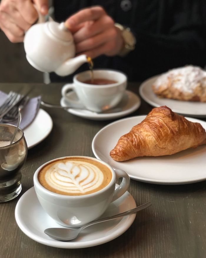 Latte art coffee cups and pastries on café table with hands reaching for drinks