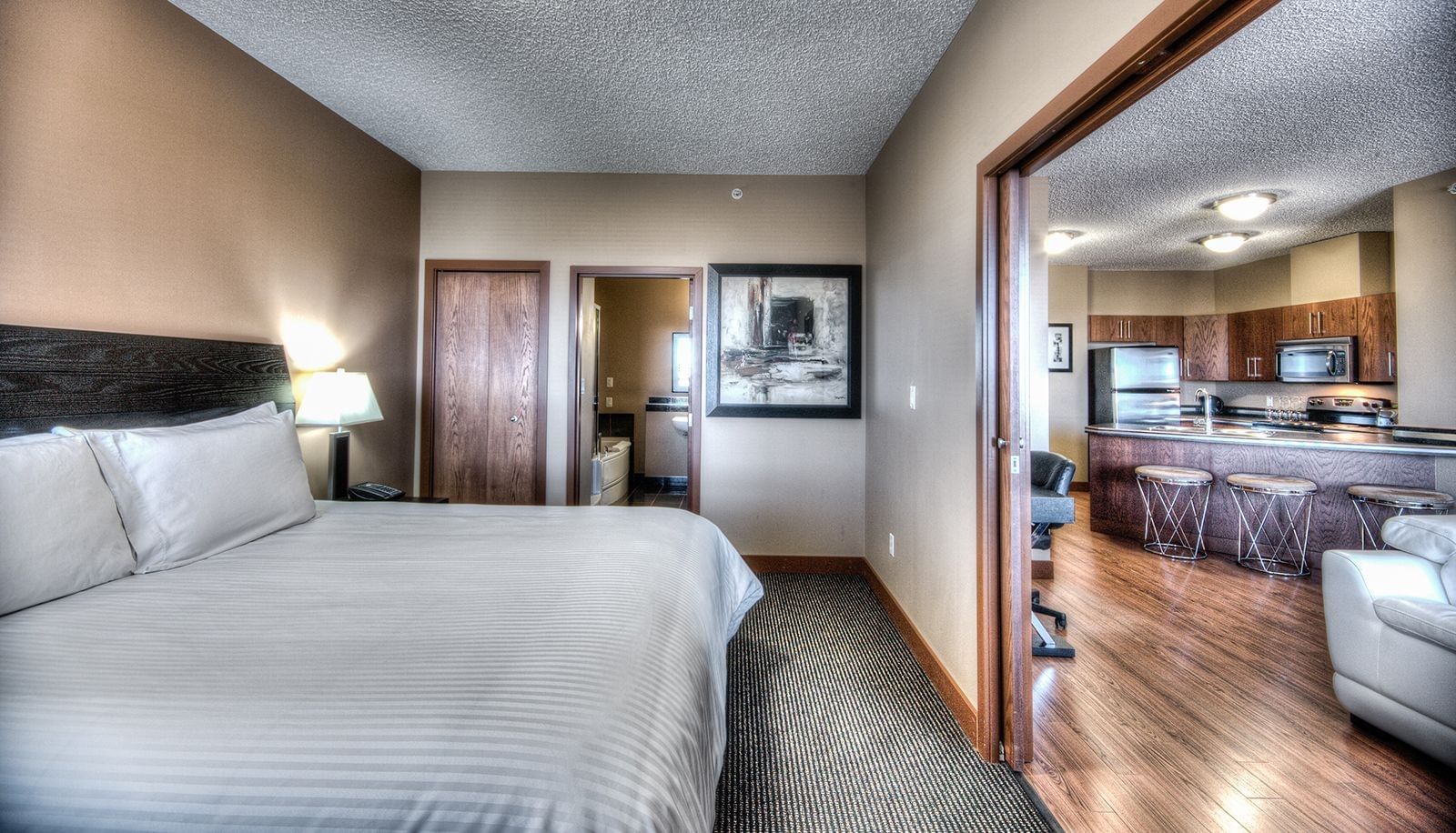 Grande Prairie Two-Bedroom Condo Suite featuring a white striped bed and a view into a full kitchen at Grand Inn & Residence