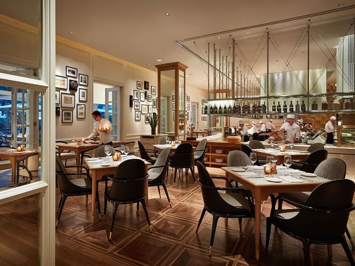 An opera interior with wooden tables, stylish chairs, and chefs working in an open kitchen at Park Hyatt Saigon