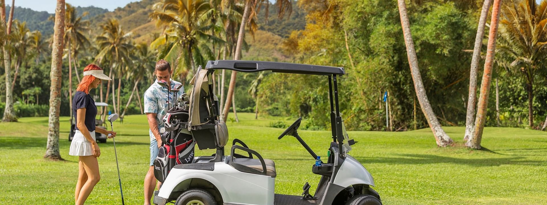 Silver golf cart by a couple with clubs under a canopy of tropical palms at The Naviti Resort - Fiji