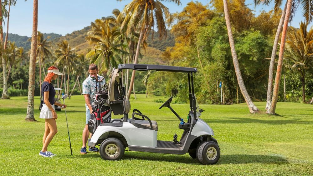 Silver golf cart by a couple with clubs under a canopy of tropical palms at The Naviti Resort - Fiji