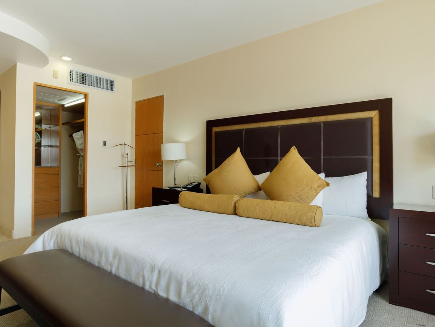 King Presidential Suite featuring a dark wood headboard, yellow pillows, and a private closet at Real Inn Torreon