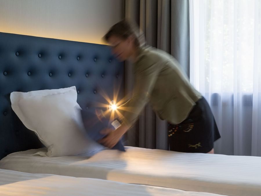 A maid preparing a bed in a room at Hotel Les Caps