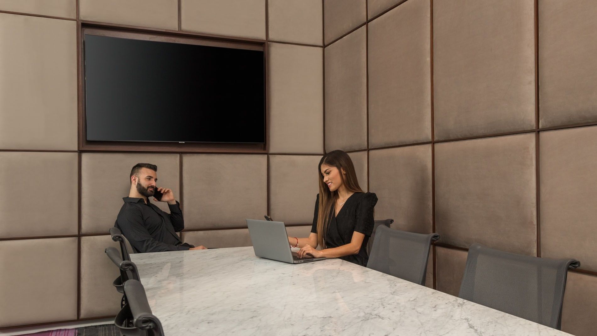 Business guests working on laptops in a modern, padded-wall meeting room facility at Camino Real Merida