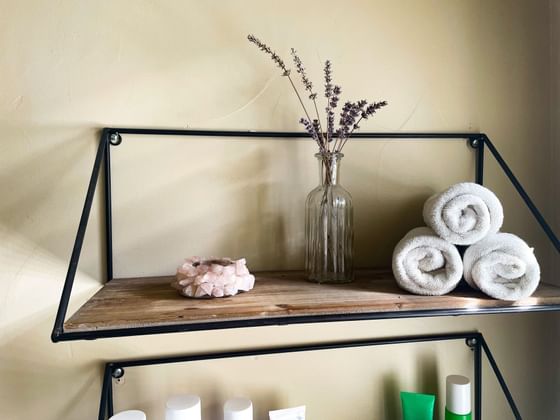 Black metal shelf with lavender, towels, and a crystal holder, above another shelf with various containers.