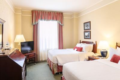 Two beds with striped curtains by a large window under warm lamps in Standard Room Two Double at Rodd Charlottetown Hotel