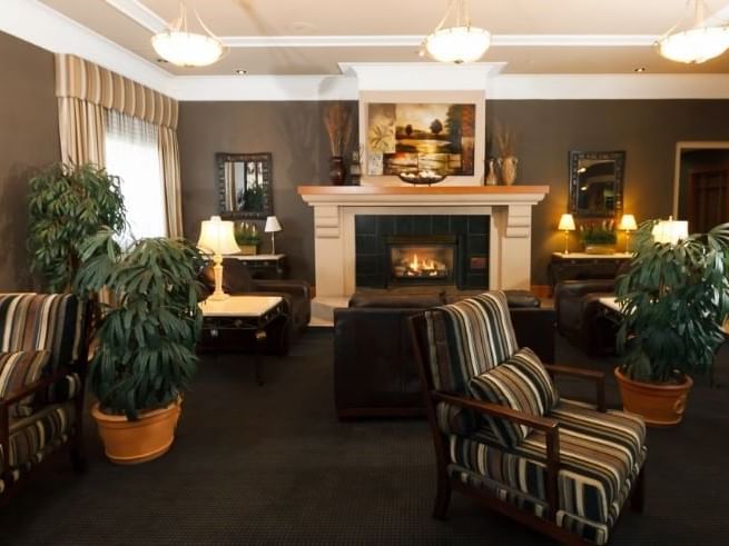 Illuminated lounge area with arranged seating and plant decor with a fireplace nearby at The Glenmore Inn & Convention Centre