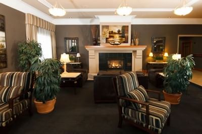 Lounge seating with striped armchairs by a fireplace, surrounded by potted plants at Glenmore Inn & Convention Centre