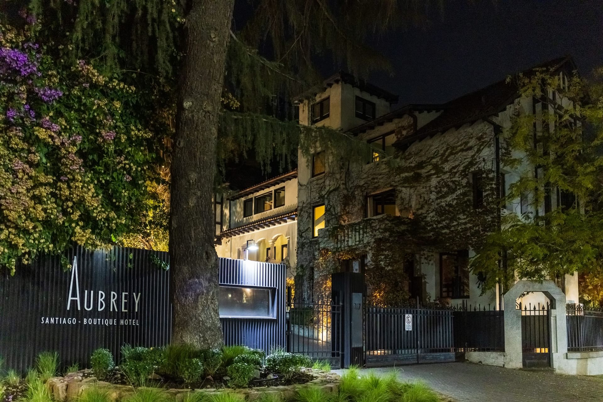 La entrada iluminada del Hotel Aubrey de noche, con su cartel y portón visibles, hoteles en Bellavista Santiago Chile