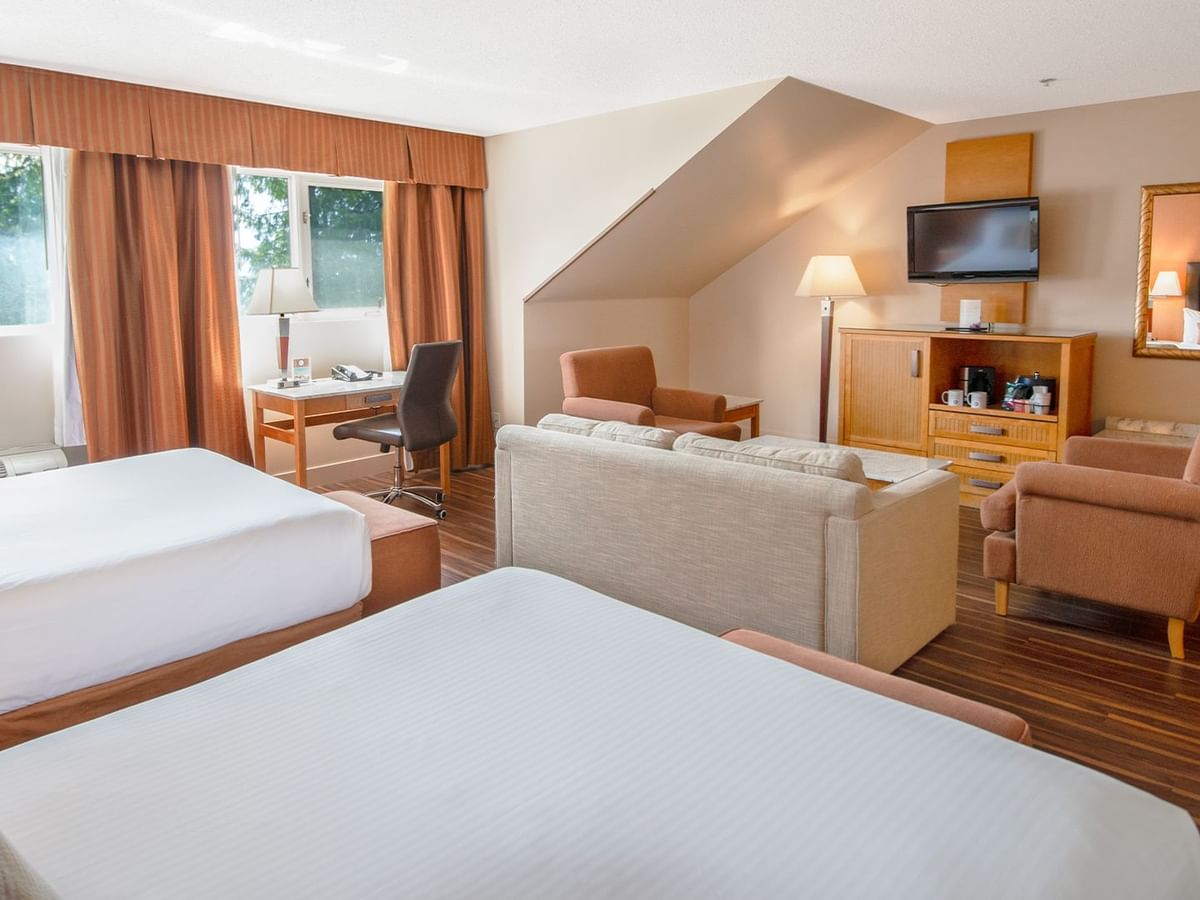 Hotel guest room with two queen beds, arm chairs, and TV