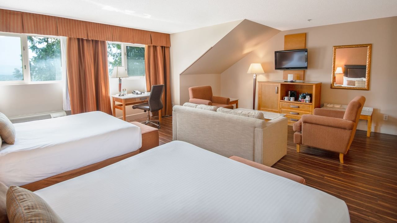 Hotel guest room with two queen beds, arm chairs, and TV