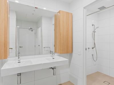 Modern bathroom with white tiles, two sinks, wooden cabinets, and a walk-in shower at UniLodge Brisbane City.