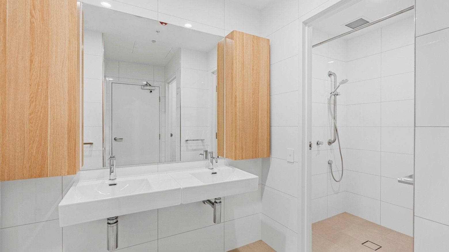 Modern bathroom with white tiles, two sinks, wooden cabinets, and a walk-in shower at UniLodge Brisbane City.