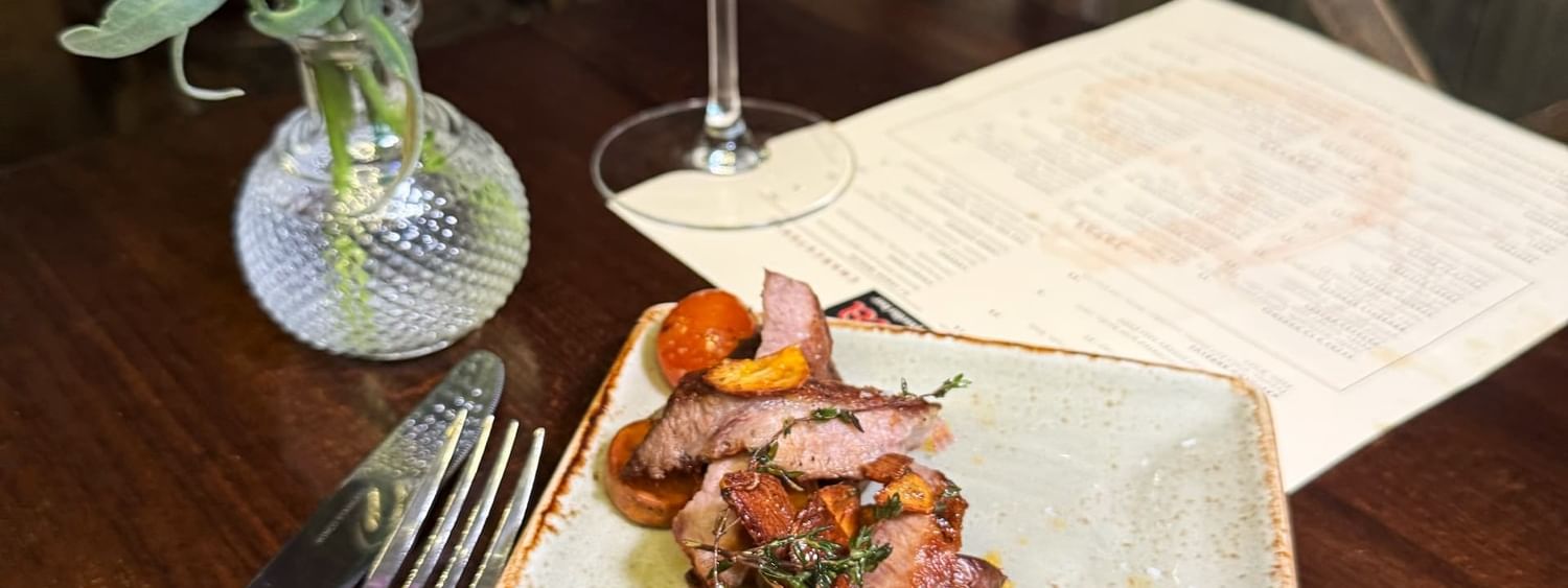 Sliced steak by purple flowers and a glass of wine on a dark table in BOTA at Warwick San Francisco