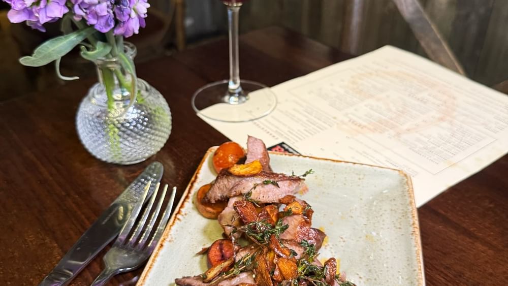 Sliced steak by purple flowers and a glass of wine on a dark table in BOTA at Warwick San Francisco