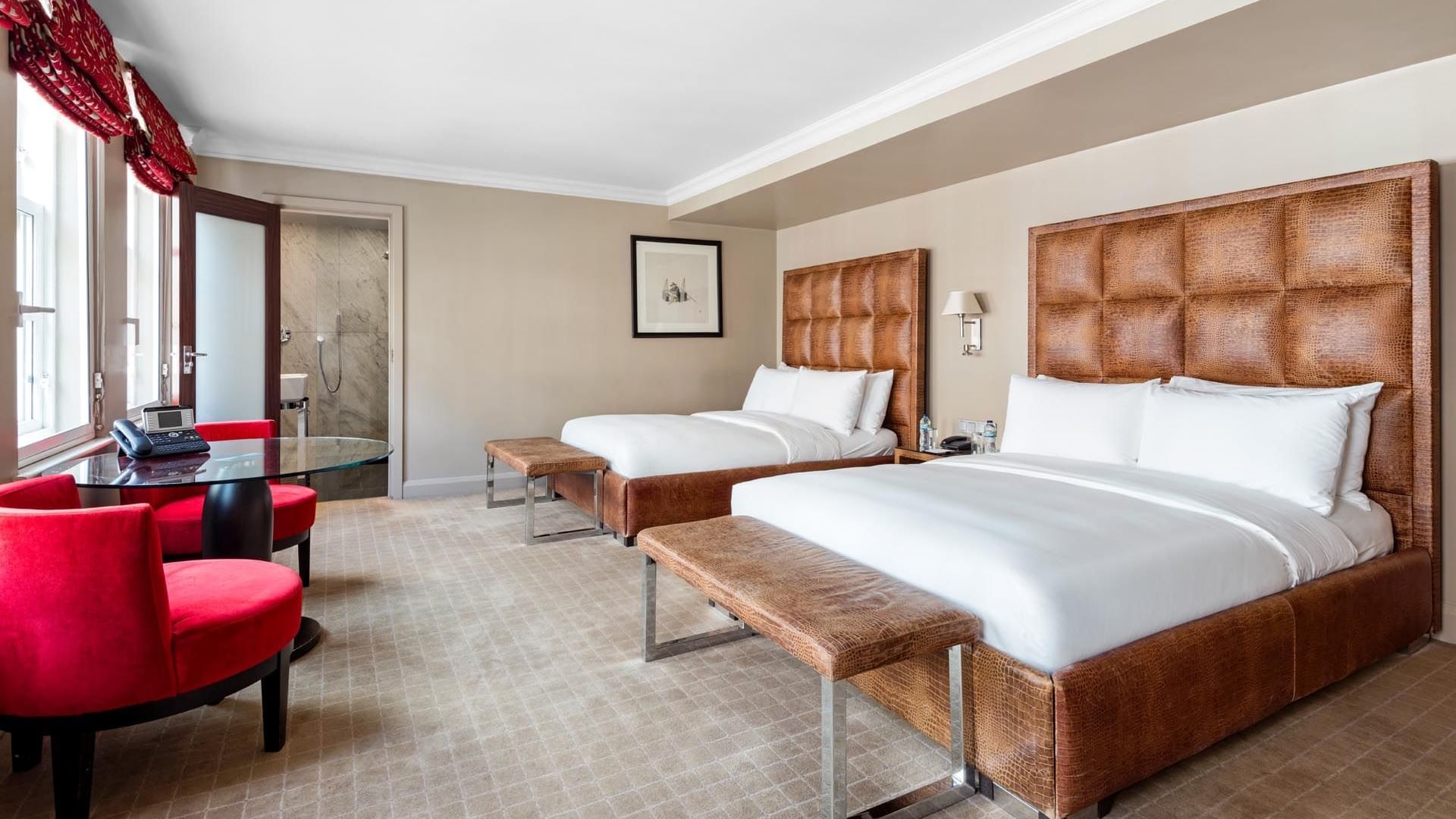 Spacious Family Room at The May Fair Hotel London with two double beds, wooden benches, red chairs, and a glass table