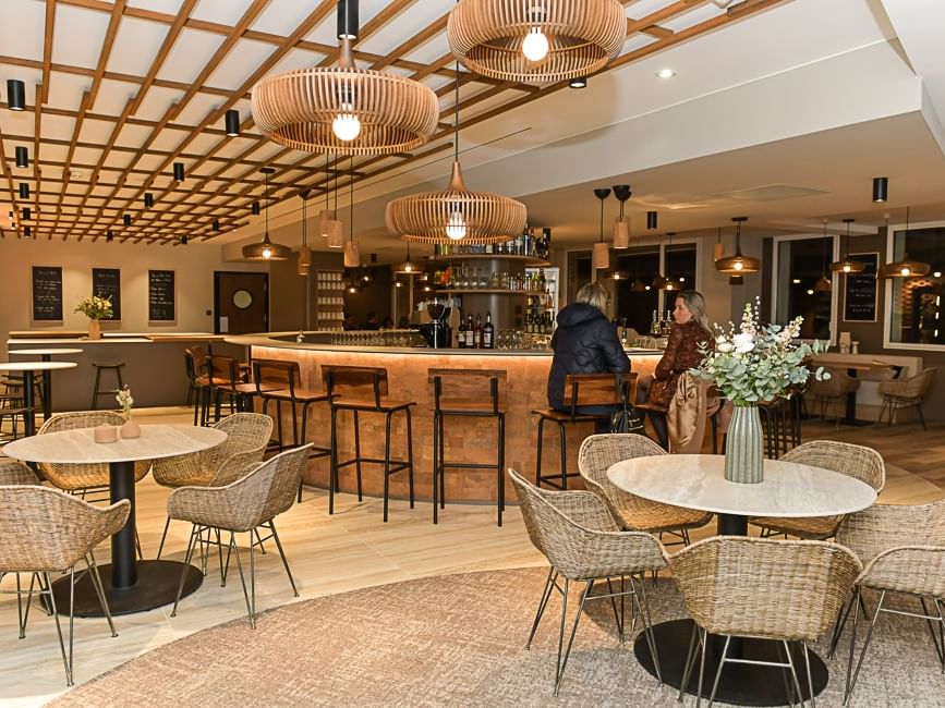 Salon élégant avec tables, chaises en osier et bar à l'Hôtel Rivella.