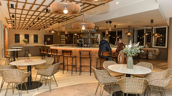 Salon élégant avec tables, chaises en osier et bar à l'Hôtel Rivella.