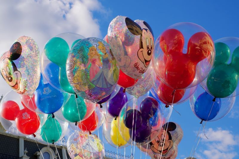 A collection of balloons in colors like blue, red, and translucent, featuring Mickey Mouse and other Disney characters. 