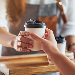 A waitress handing customers two paper cups of coffee