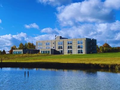 Exterior view of Avaneo Hotel Marktredwitz reflected in a serene pond, surrounded by green grass and trees